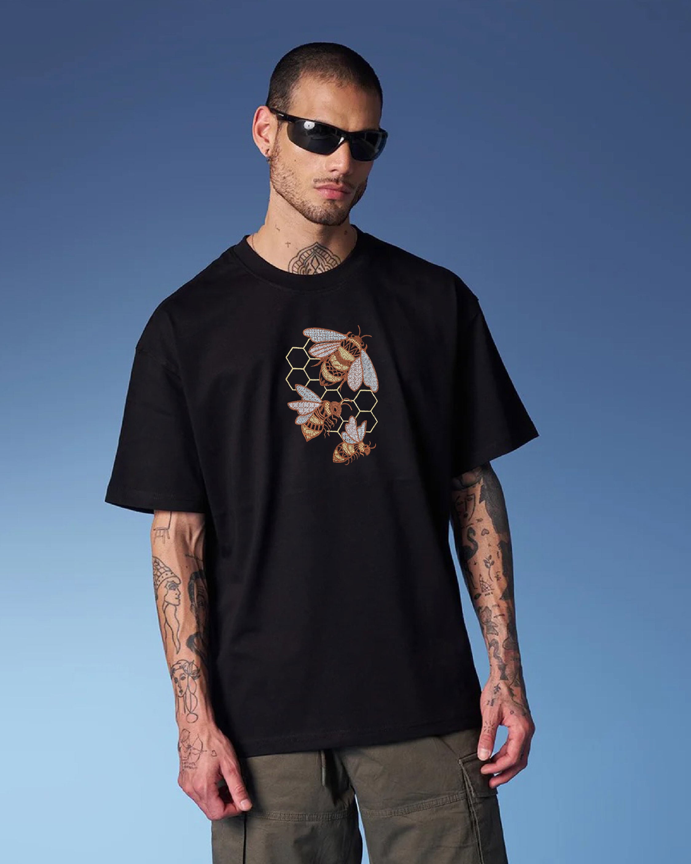 Man wearing a black t-shirt with a bee and honeycomb design against a blue sky.