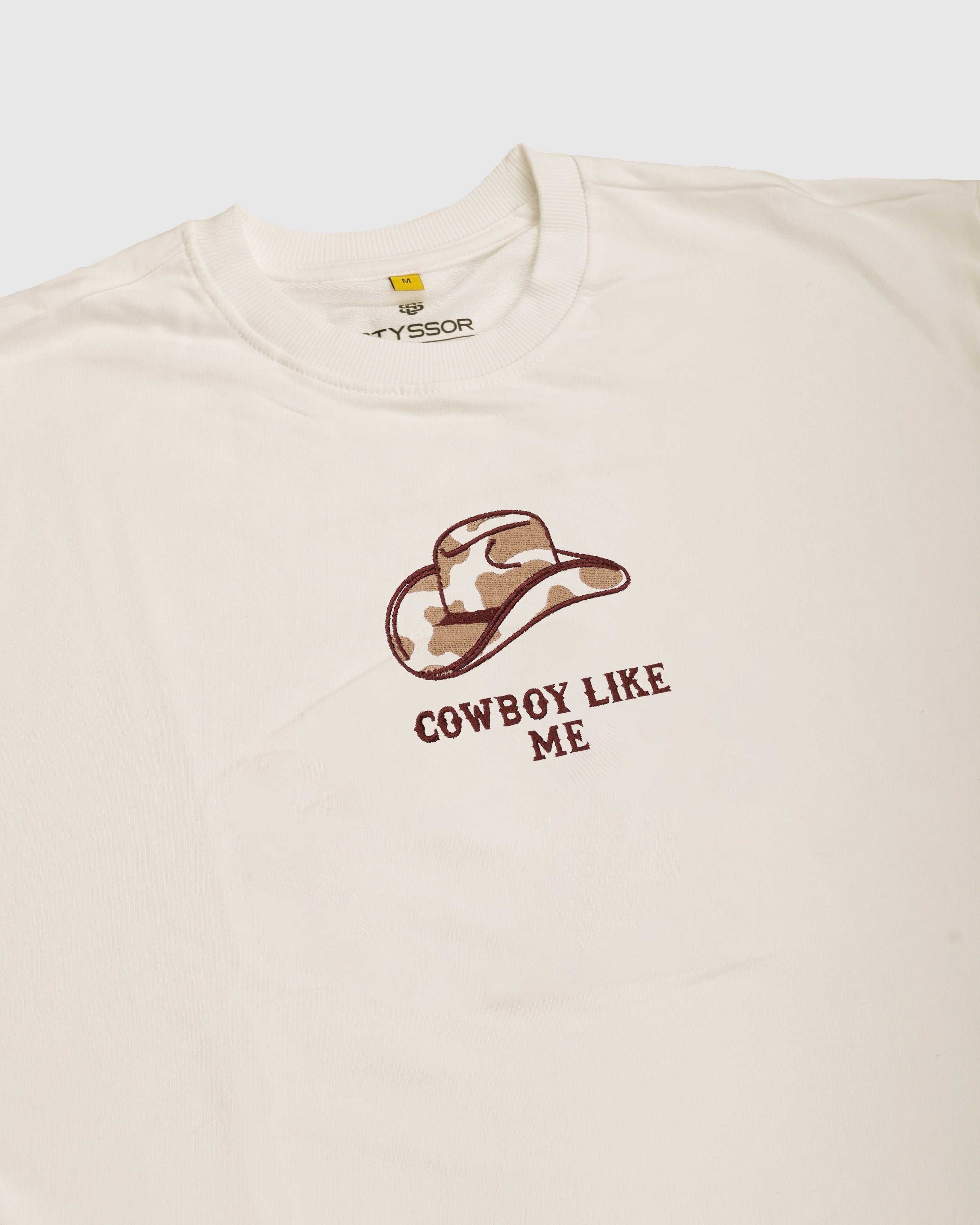 Beige t-shirt with a cowboy hat graphic and 'Cowboy Like Me' text on a white background