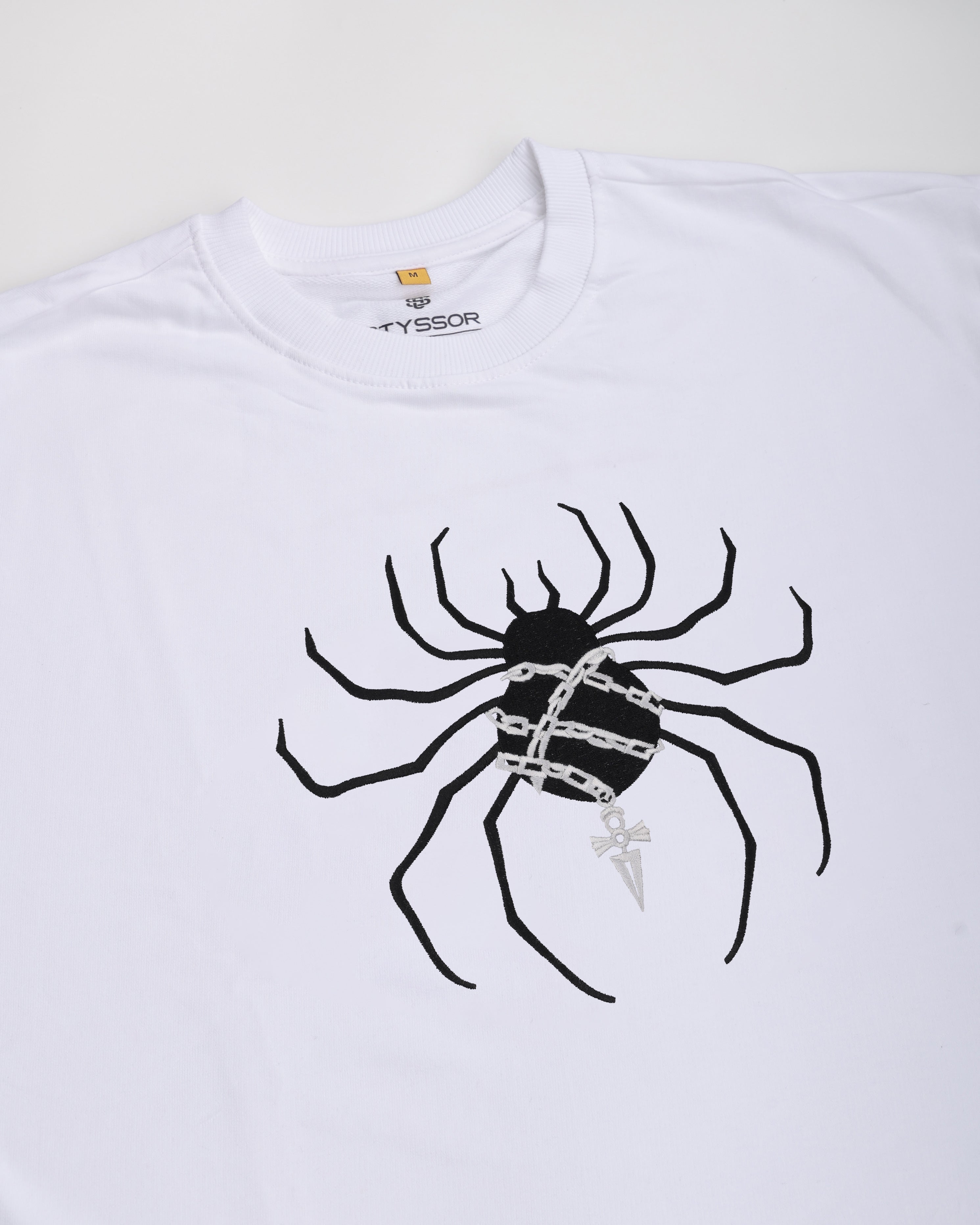 White t-shirt with a black spider graphic and 'Syssor' branding on a white background