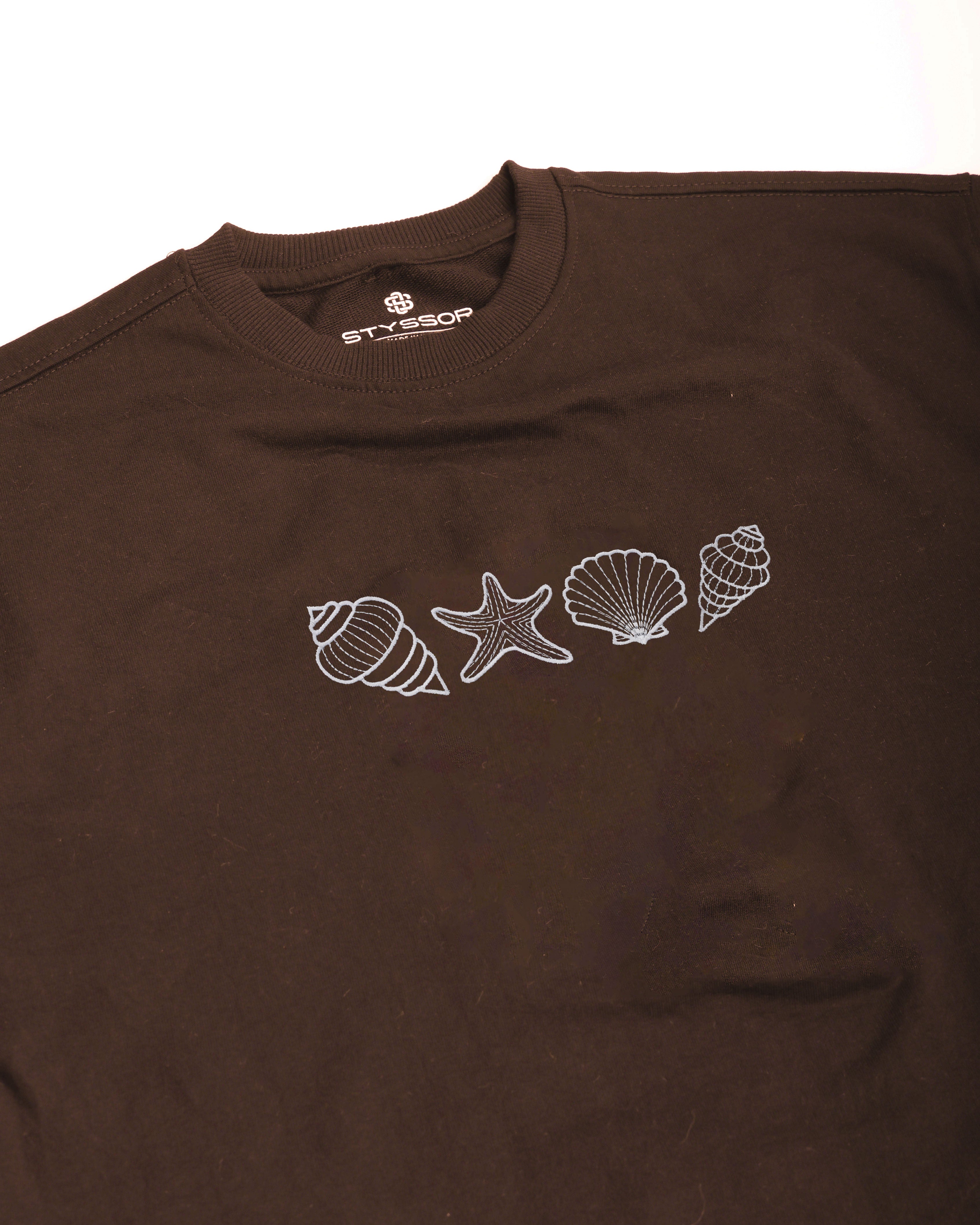 Brown t-shirt with white shell and seashell designs on a white background