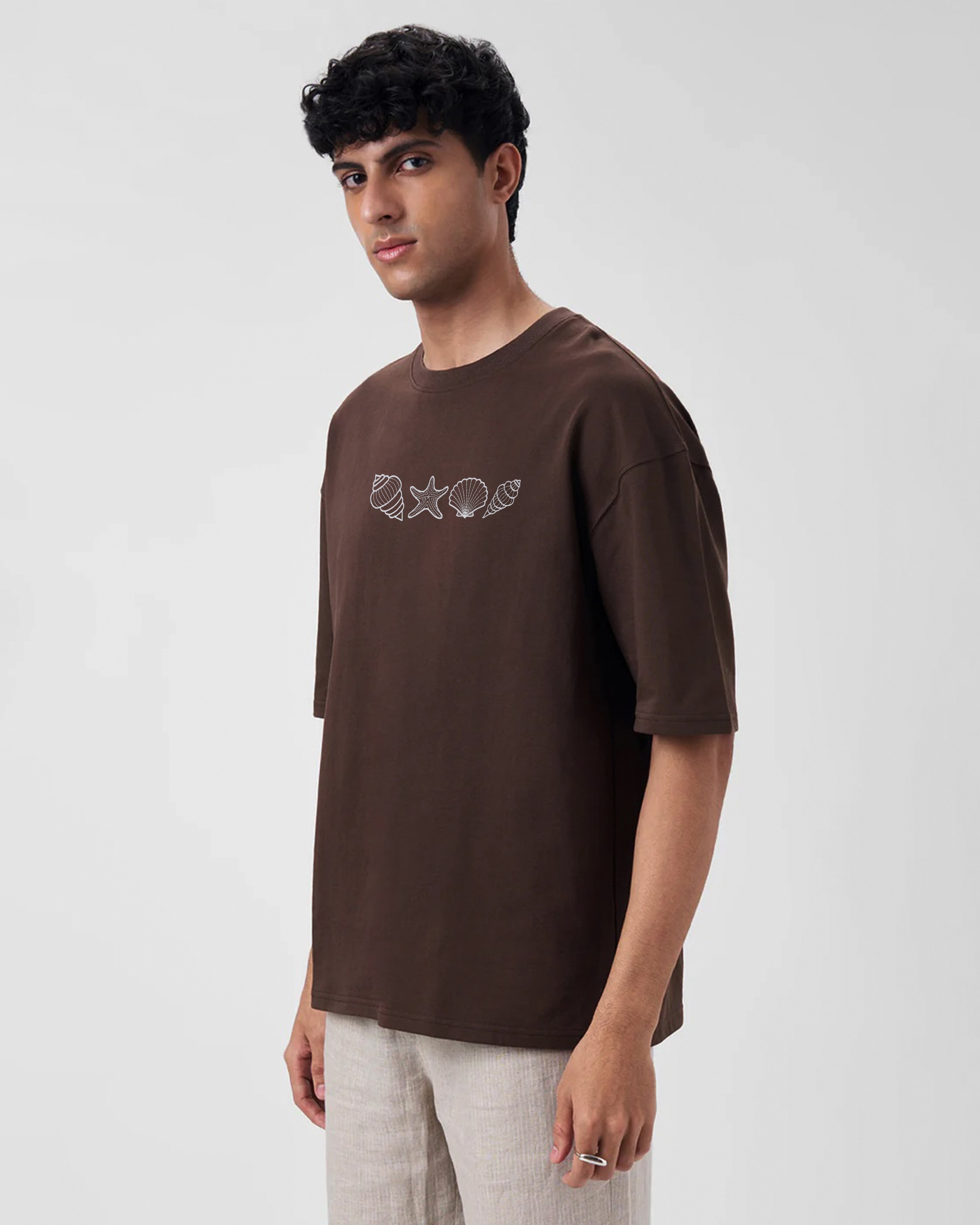 Man wearing a brown t-shirt with a embroidery design on a light gray background