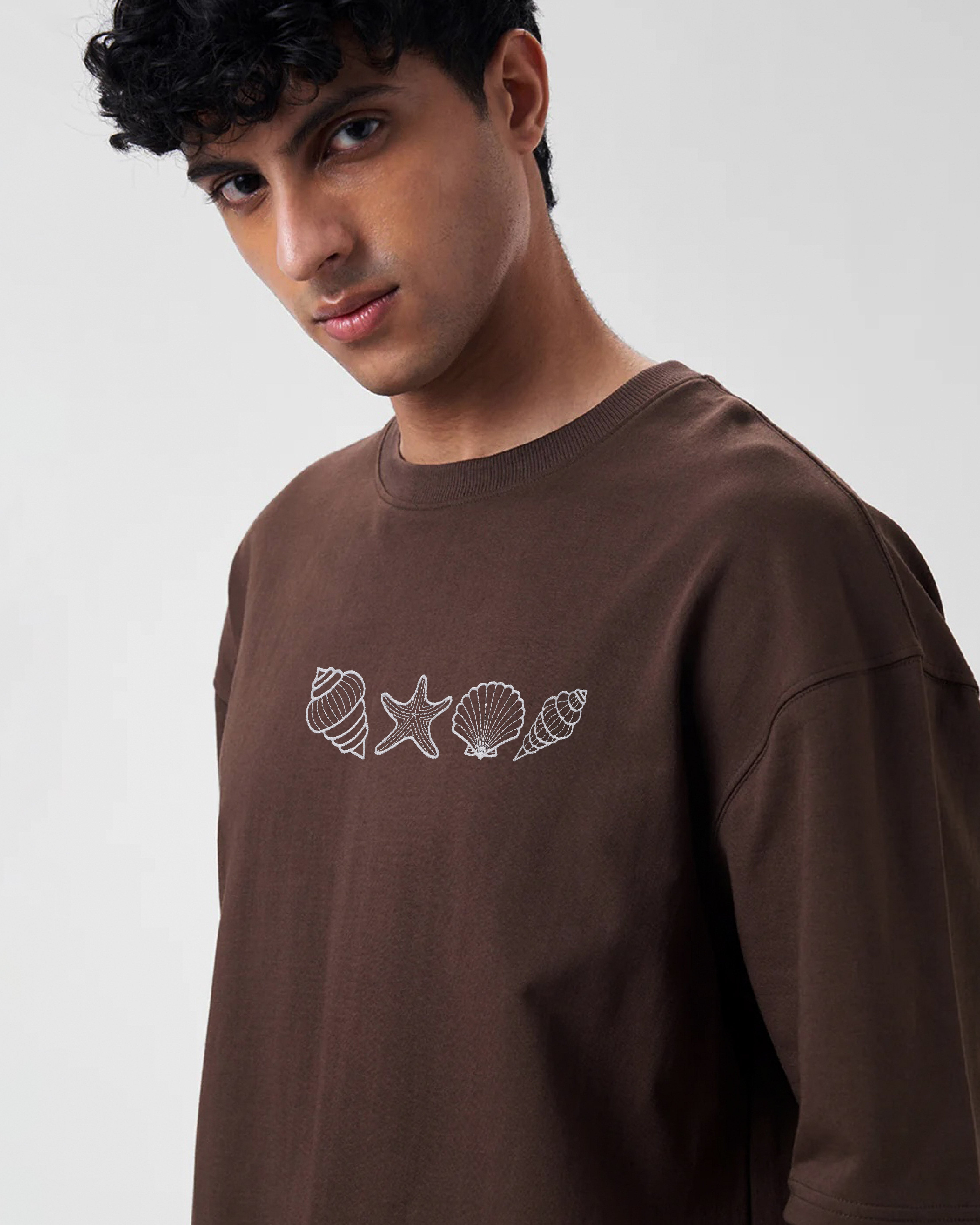Man wearing a brown long-sleeve shirt with white shell and starfish designs on a plain background