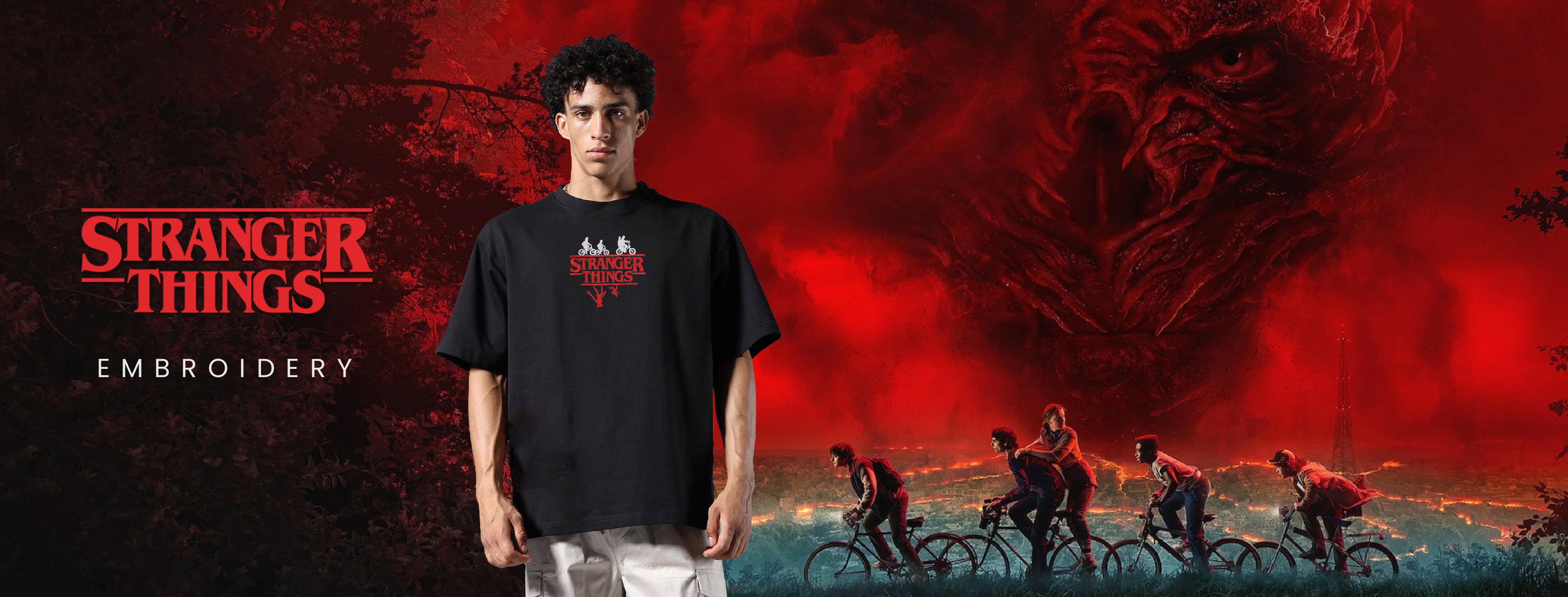 Person wearing a black t-shirt with embroidery design in front of a Stranger Things-themed background.