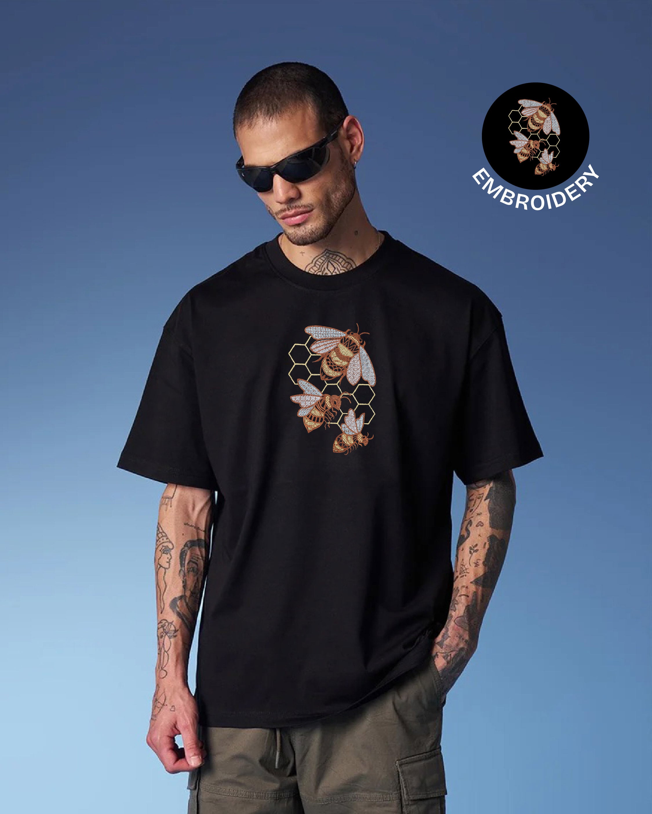 Man wearing a black t-shirt with a bee and honeycomb design against a blue sky.