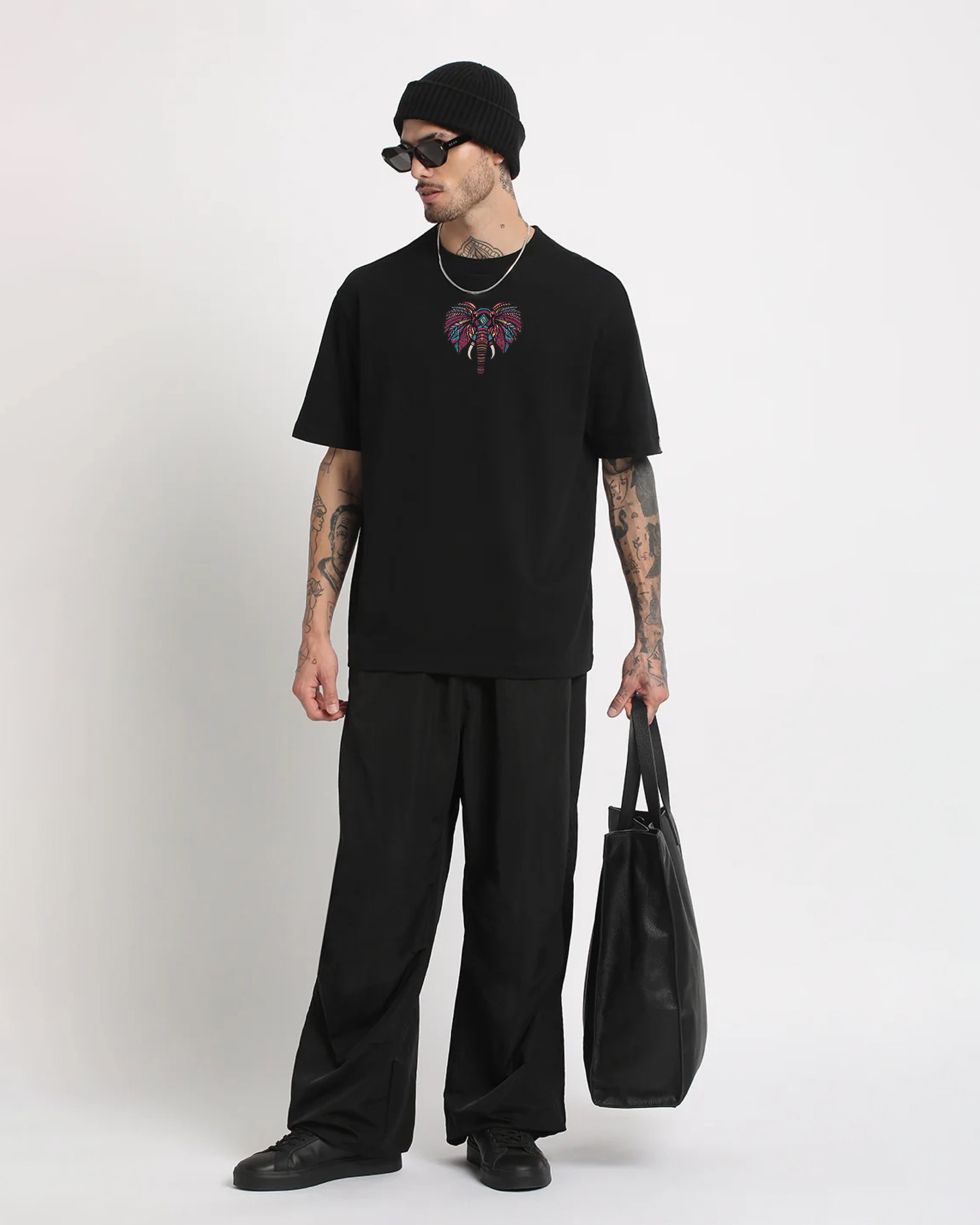 Man wearing a black t-shirt with a colorful design, holding a black bag on a white background