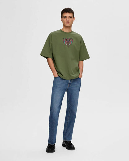 Person wearing a green t-shirt with a colorful elephant design and blue jeans on a white background