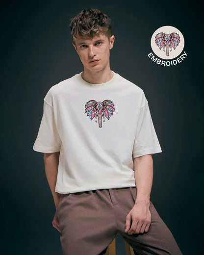 Man wearing a white t-shirt with an embroidered elephant design on a dark background