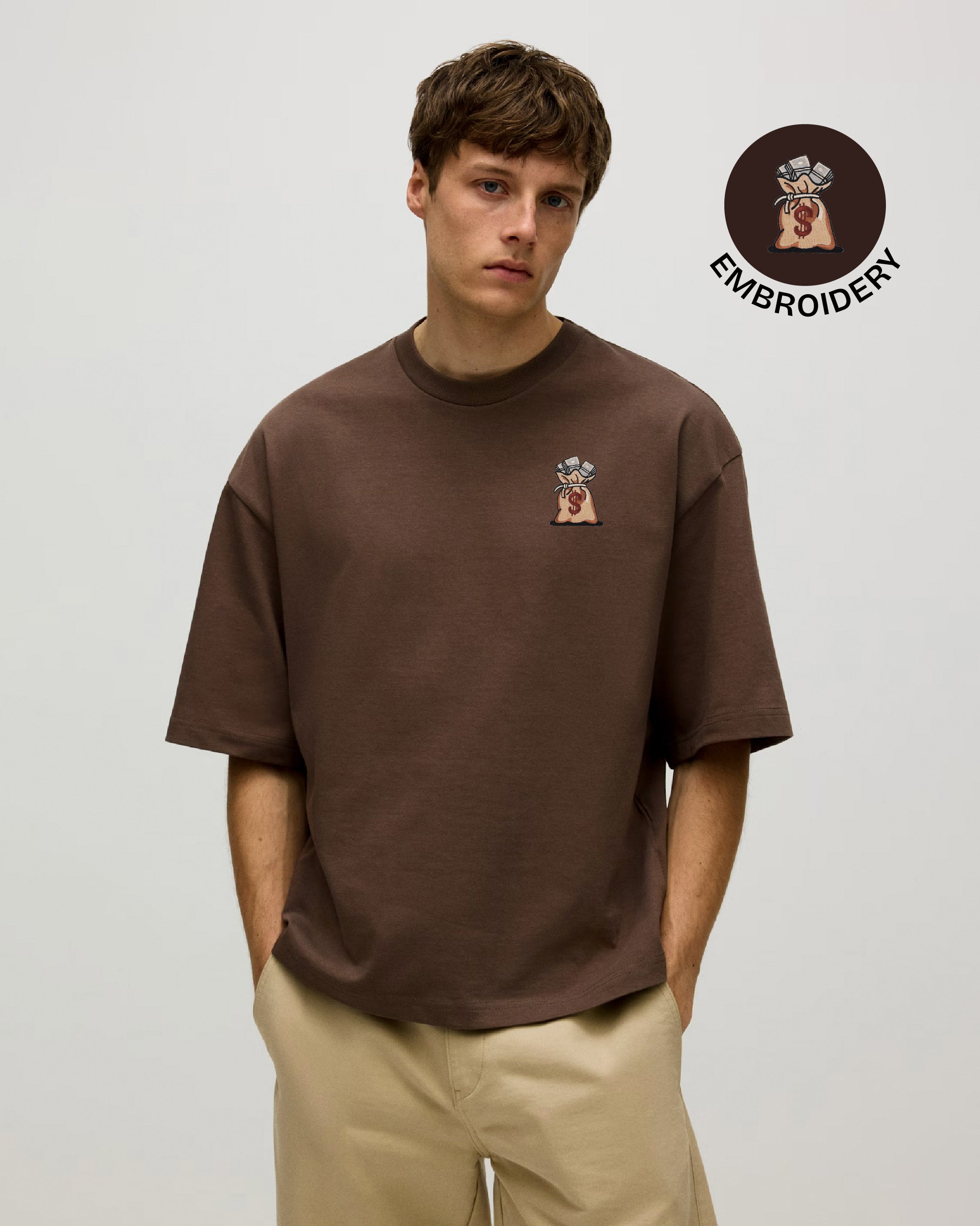 Man wearing a brown t-shirt with a small embroidered design on a light gray background