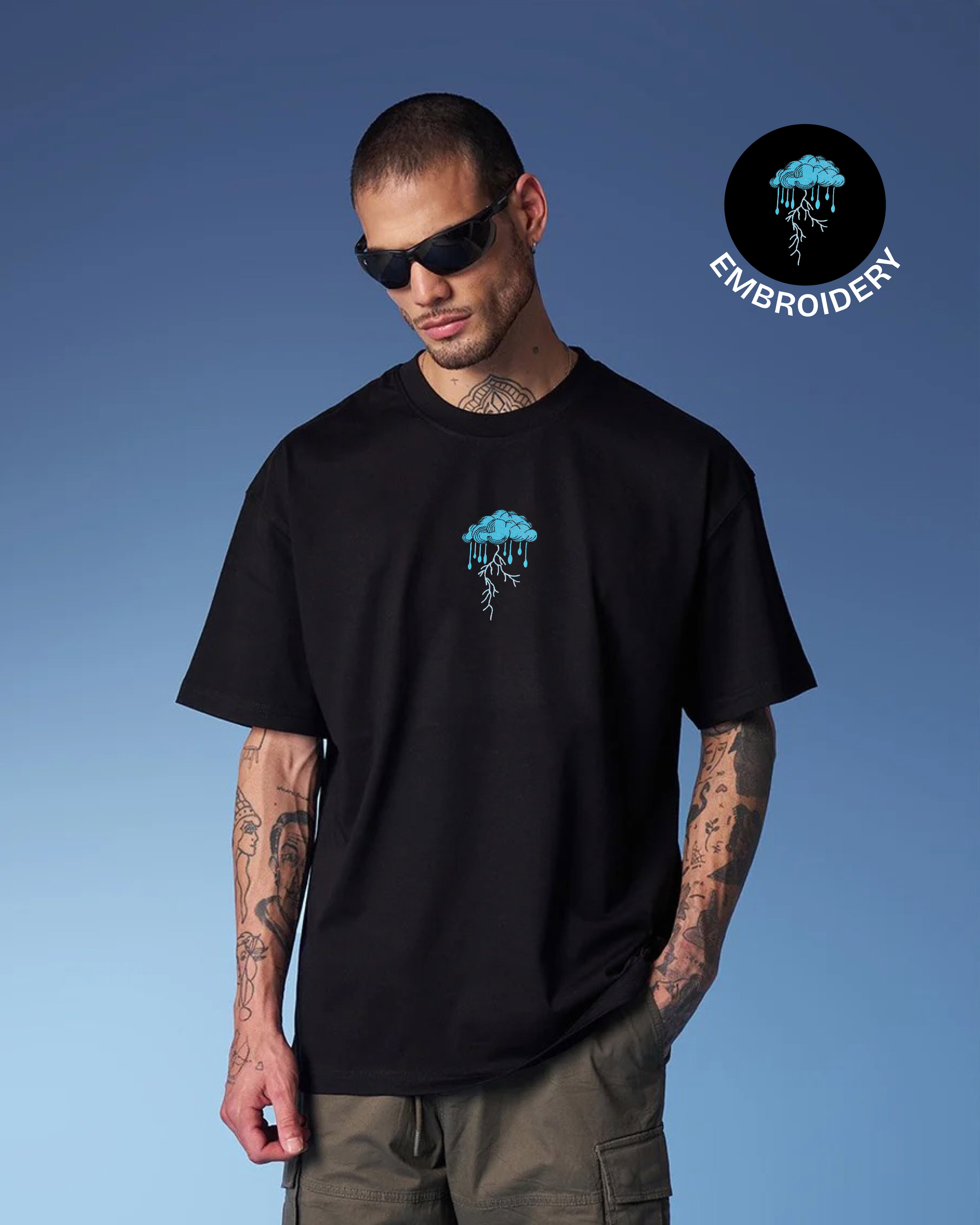Man wearing a black t-shirt with blue embroidery against a blue background
