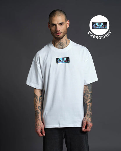 Man wearing a white t-shirt with a logo, standing against a dark background with embroidery logo overlay.