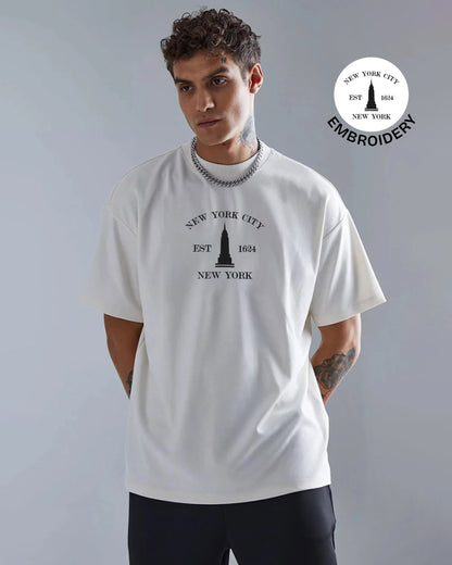 Man wearing a white t-shirt with New York City design, standing against a gray background.