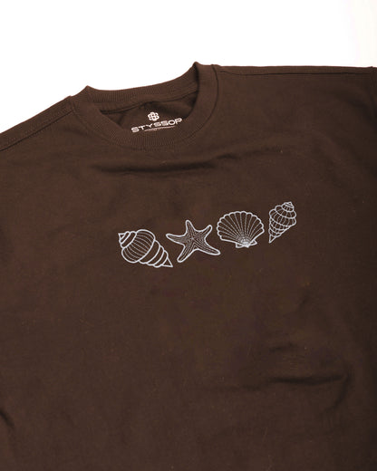 Brown t-shirt with white shell and seashell designs on a white background