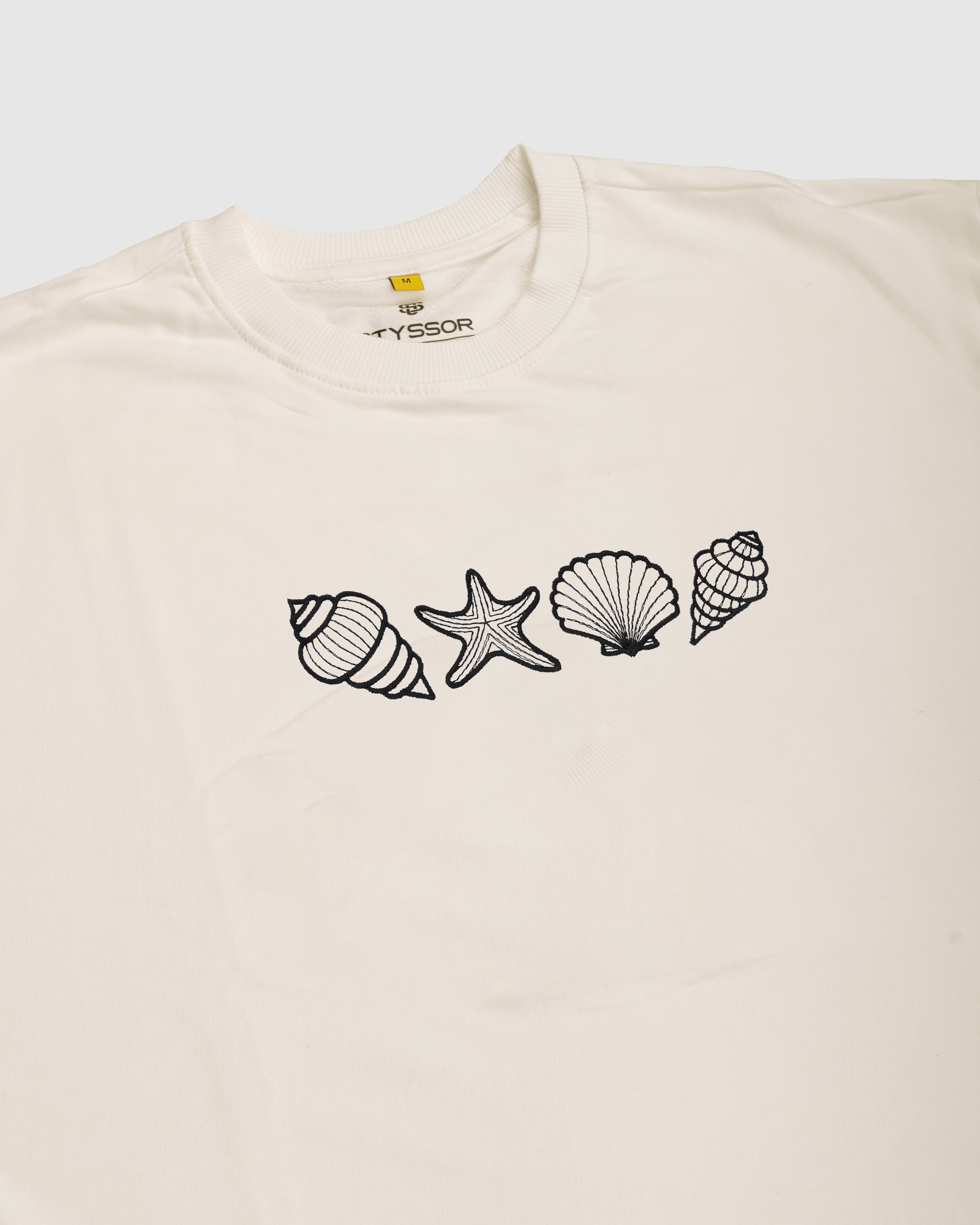 Beige t-shirt with black shell and starfish designs on a white background