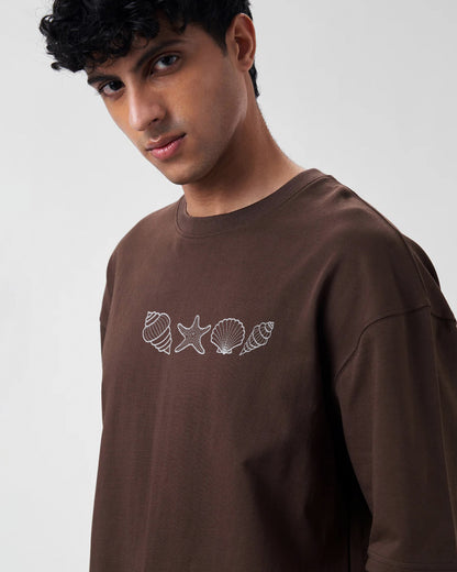 Man wearing a brown long-sleeve shirt with white shell and starfish designs on a plain background