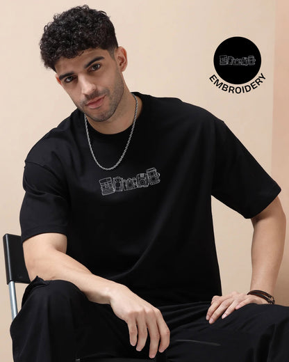 Man wearing a black t-shirt with embroidered designs on a beige background