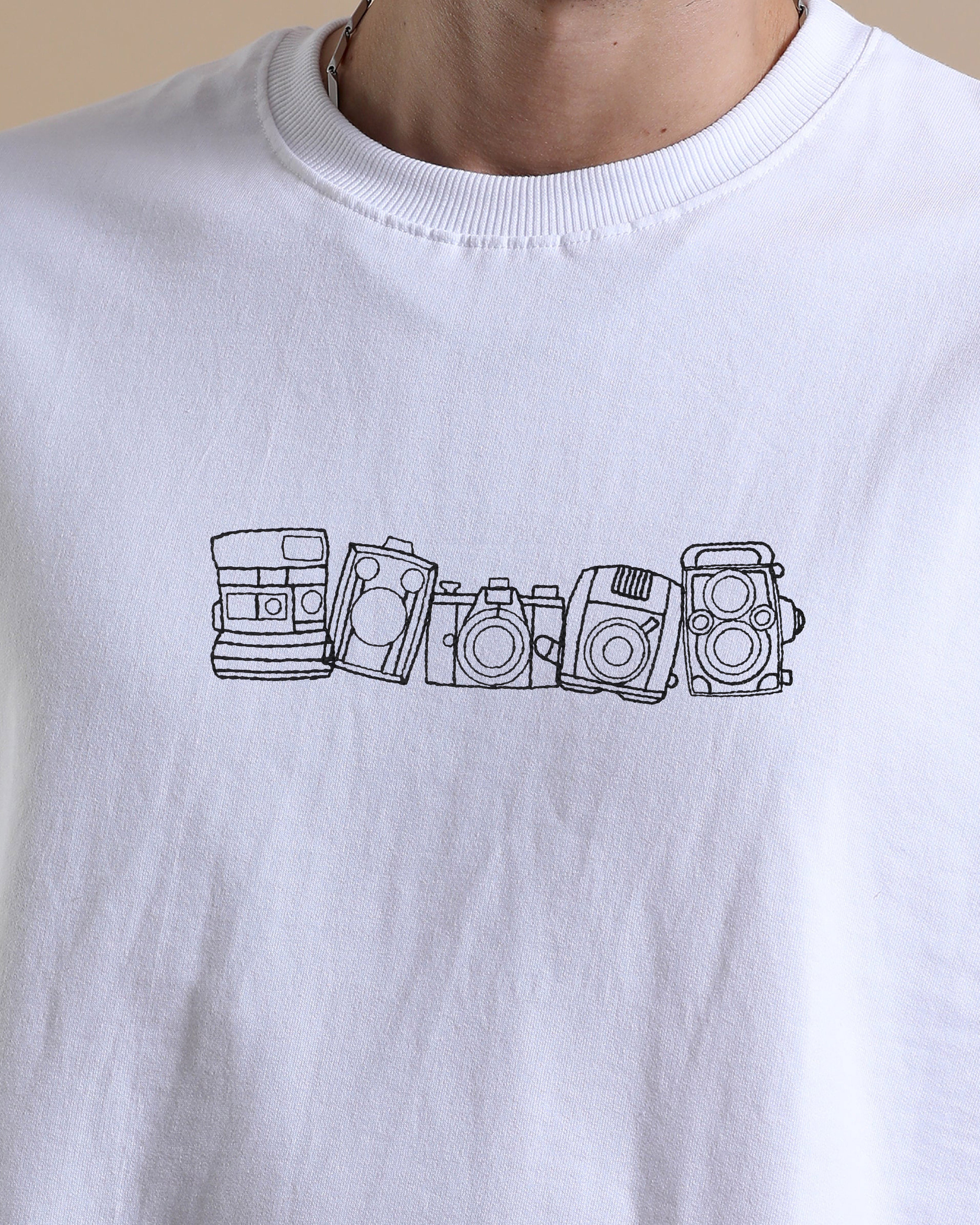 White t-shirt with black line art of five vintage cameras on a beige background